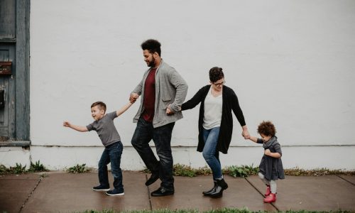 A joyful family walking together outdoors, holding hands in a playful and happy moment.