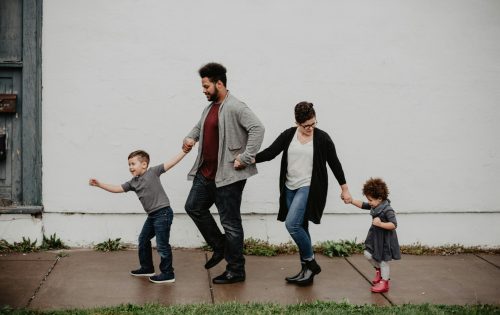 A joyful family walking together outdoors, holding hands in a playful and happy moment.
